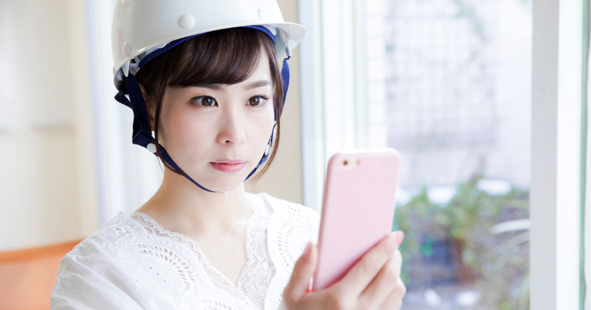 スマホを見ているヘルメットをかぶった女性の写真