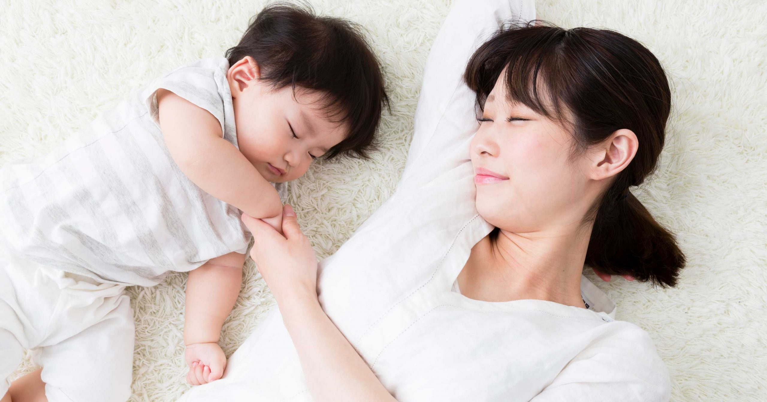 じゅうたんの上で寝転がる赤ちゃんと母親の写真